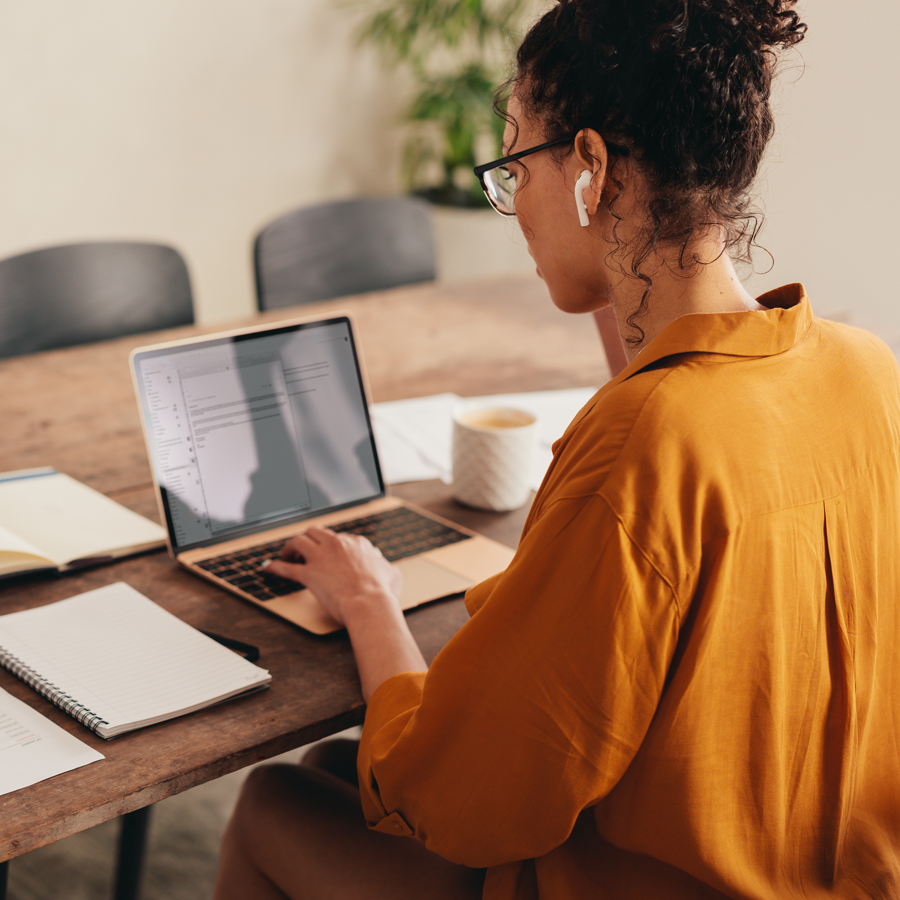 A photo taken from behind a woman who is on a laptop at at a desk