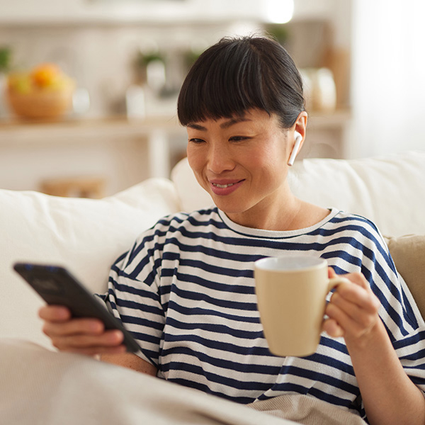 An Asian woman using mobile phone while enjoying coffee at home