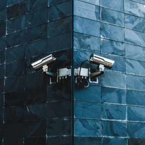 Two security cameras are seen attached to a blue brick wall.
